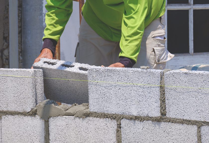 Mason setting a hollow gray block into a new course, with a string line running along the wall
