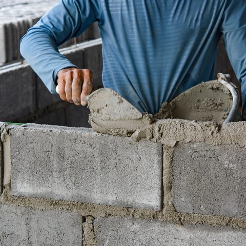 Mason spreading mortar from a trowel along the top of a gray block wall