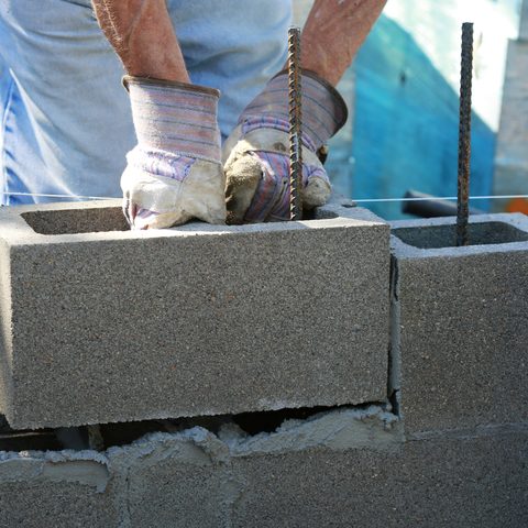 Gloved hands lowering a hollow concrete block over an upright steel bar